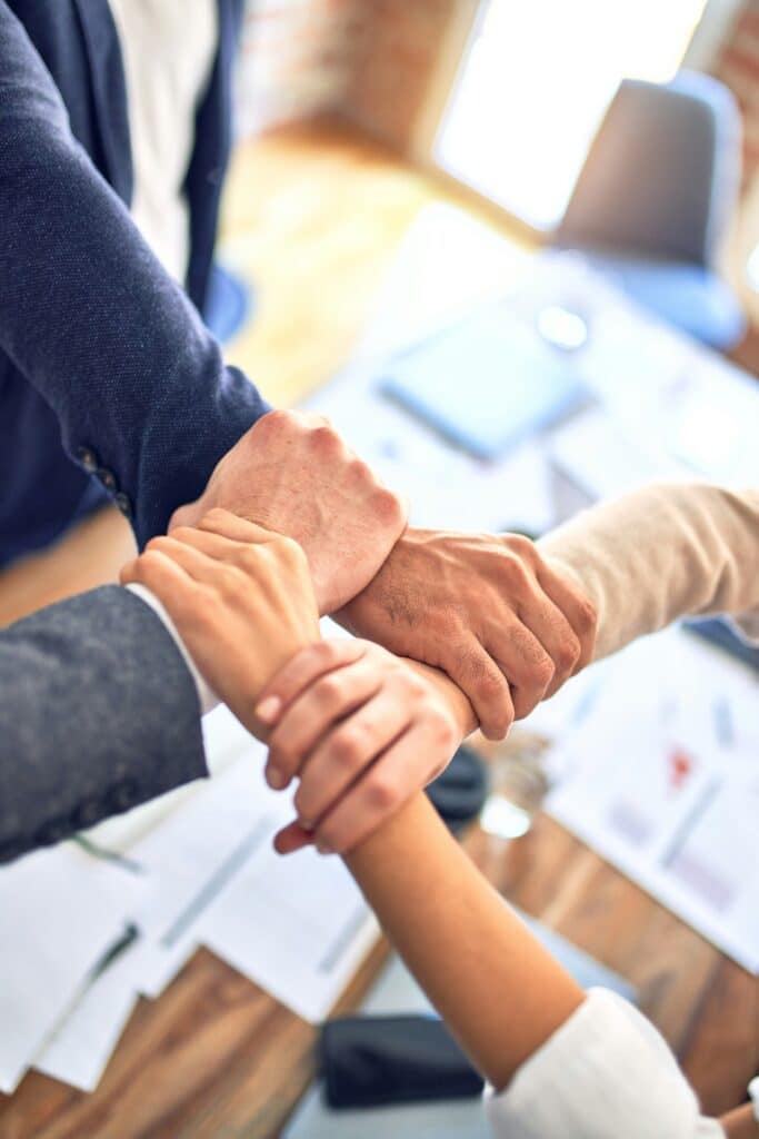Mãos de vários colegas unidas em gesto de parceria, simbolizando liderança e comunicação em equipa.
